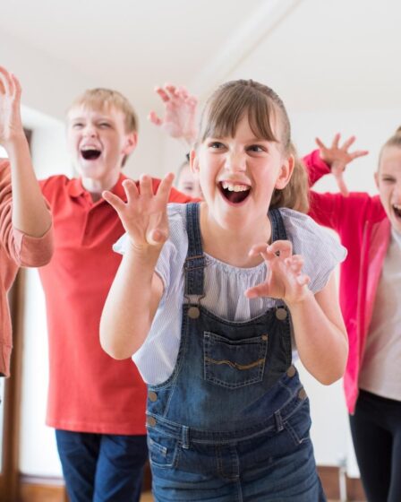 Four children indoors laugh and pretend to be scary monsters, raising their hands with clawed fingers and playful expressions. This lively scene highlights how sensory activities can spark creativity and fun, catering to various children's sensory needs.