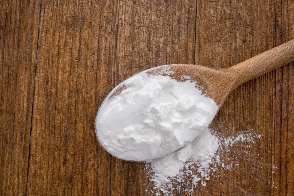 A spoonful of cornflour sits on a wooden surface, ready for your next baking or cooking adventure.