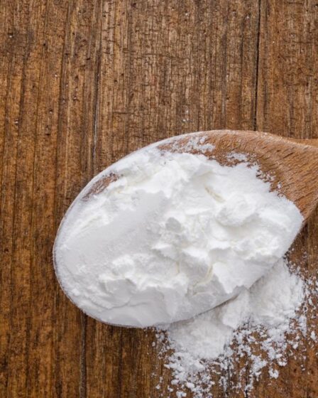 A spoonful of cornflour sits on a wooden surface, ready for your next baking or cooking adventure.