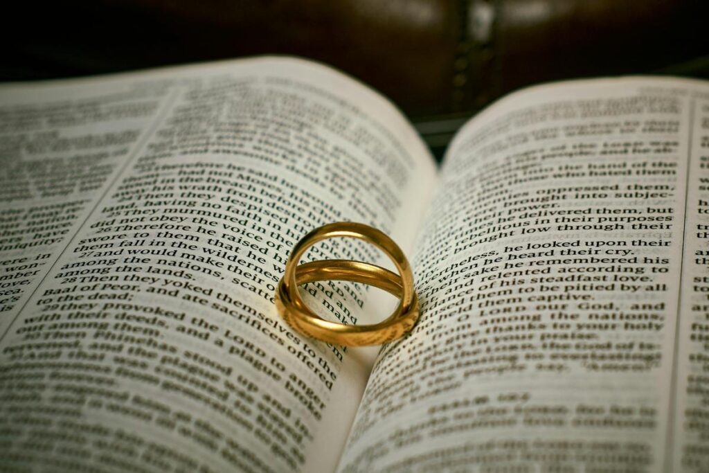 Two gold rings rest on an open Bible, forming a heart-shaped shadow—symbolising love, marriage, and the bond couples share. The lighting highlights the rings and text, capturing a moment cherished in Christian dating journeys.