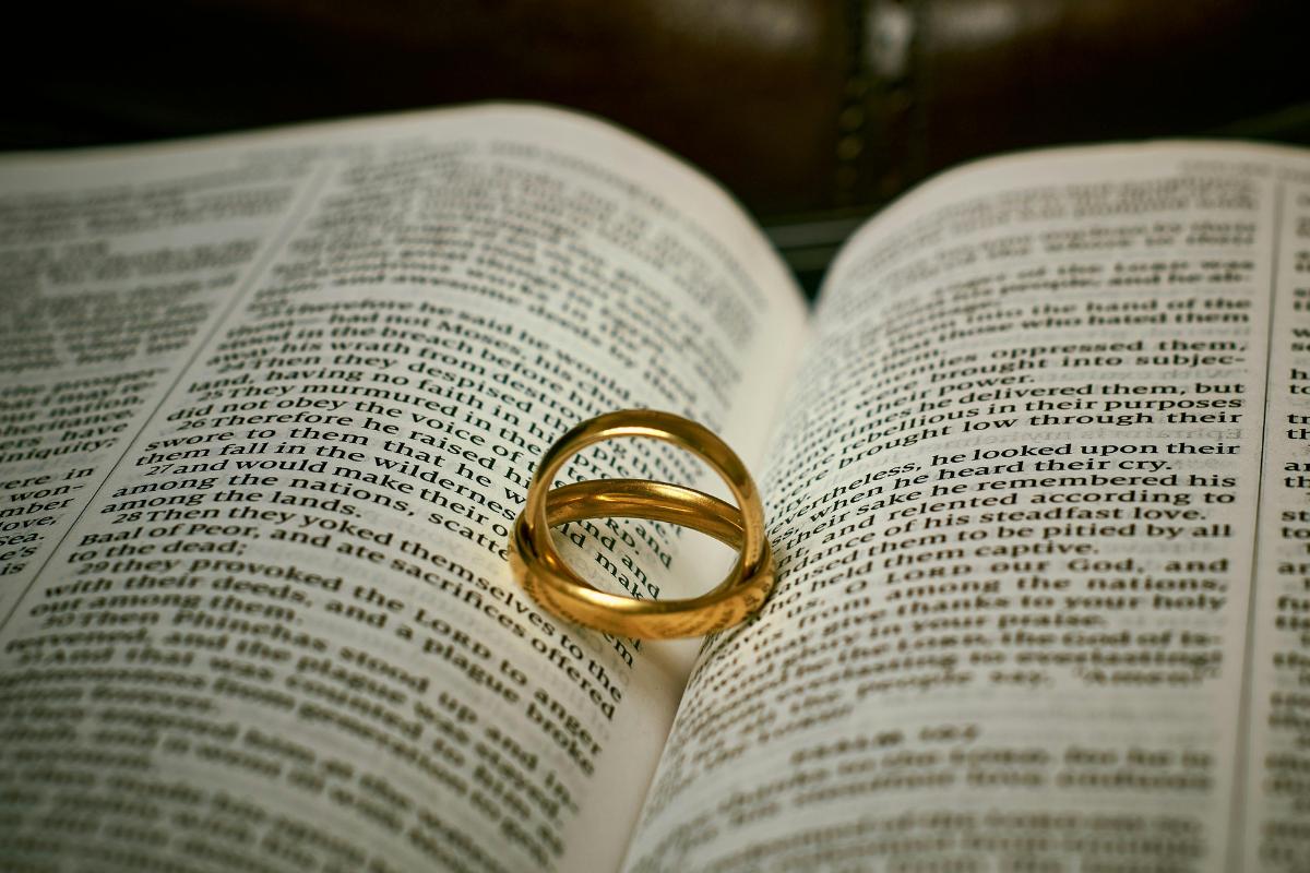 Two gold rings rest on an open Bible, forming a heart-shaped shadow—symbolising love, marriage, and the bond couples share. The lighting highlights the rings and text, capturing a moment cherished in Christian dating journeys.