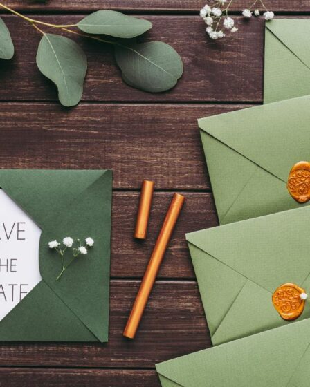A “Save the Date” card peeks from a green envelope on a wooden table. Surrounding it are more green envelopes sealed with wax—perfect for couples seeking simple wedding hacks to save money on beautiful, budget-friendly invitations.